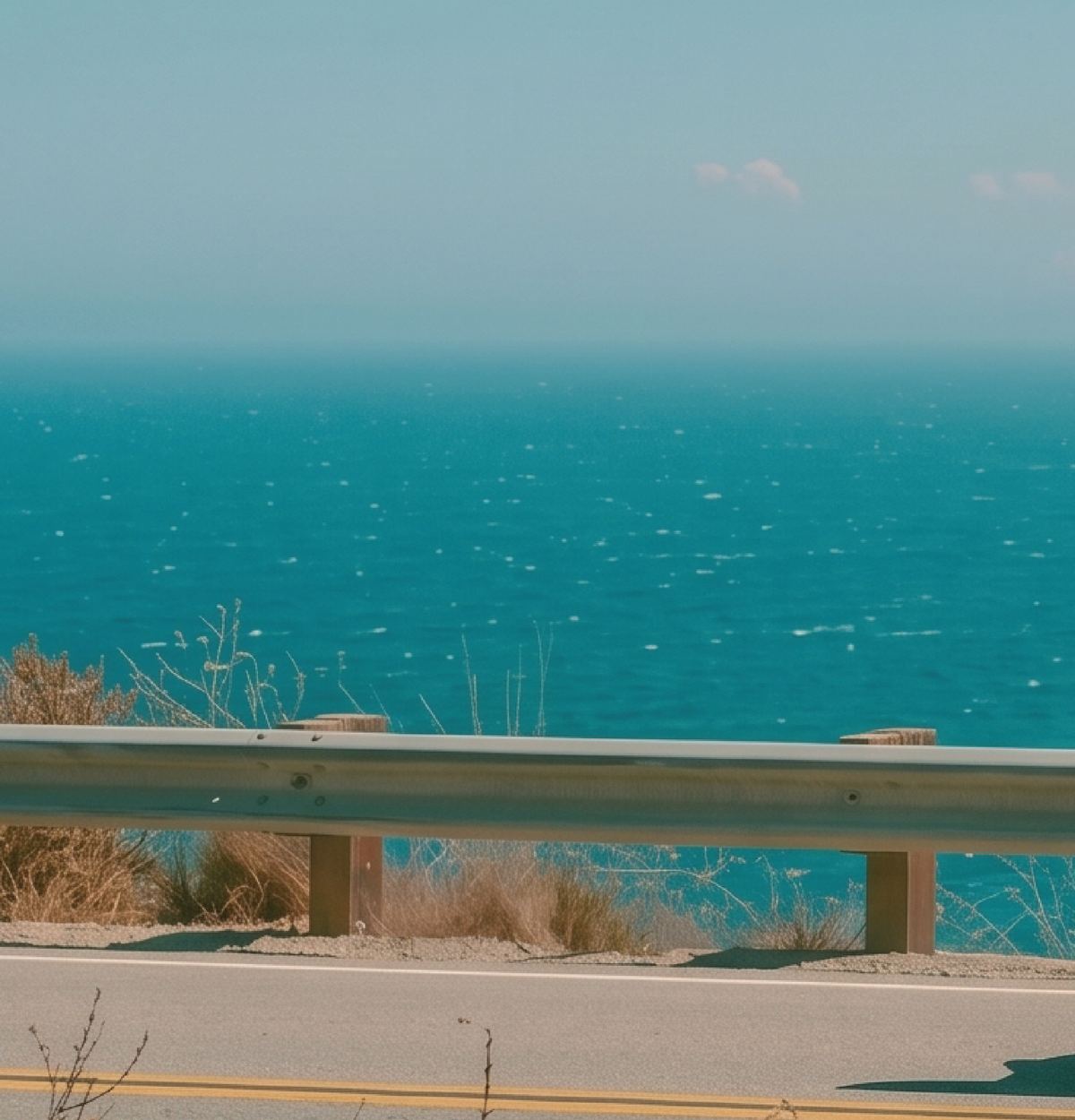 Turquoise ocean below a coastal road on a hazy summer day.